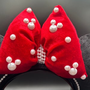K&ouml;nnte beinhalten: Rote Samt-Minnie-Maus-Ohren mit einer gro&szlig;en Schleife, die mit wei&szlig;en Perlen verziert ist.