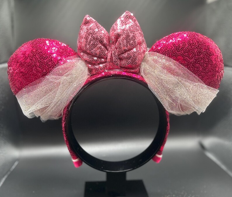 Op de afbeelding: Roze glitzerende Minnie Mouse oren haarband met een grote roze strik en witte tule.