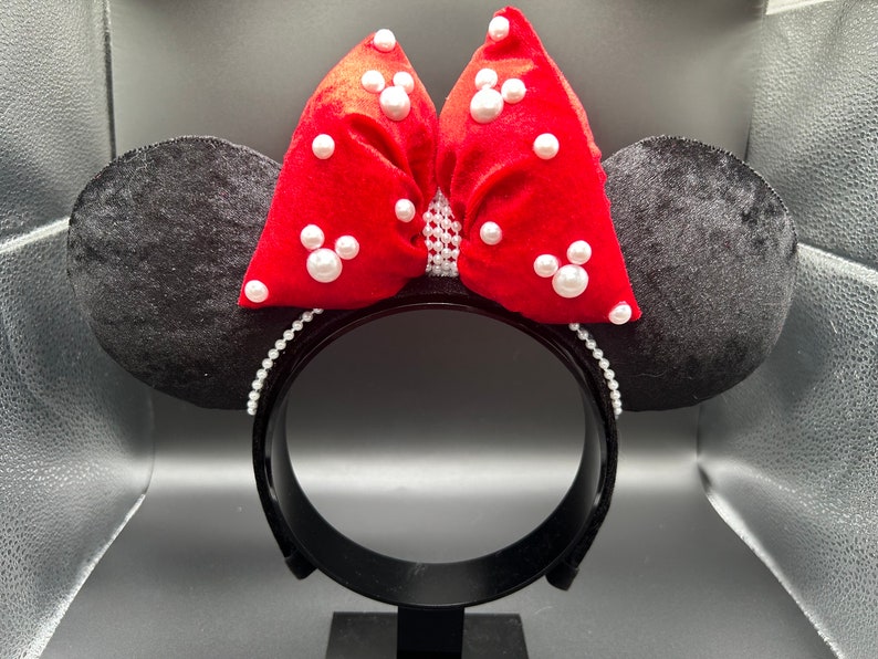 K&ouml;nnte beinhalten: Schwarze Samt-Minnie-Maus-Ohren mit einer roten Samtschleife, die mit wei&szlig;en Perlenakzenten verziert ist.