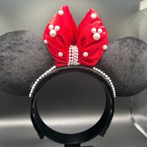 K&ouml;nnte beinhalten: Schwarze Samt-Minnie-Maus-Ohren mit einer roten Samtschleife, die mit wei&szlig;en Perlen verziert ist.