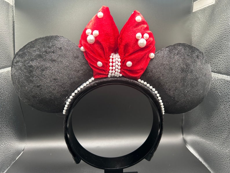 K&ouml;nnte beinhalten: Schwarze Samt-Minnie-Maus-Ohren mit einer roten Samtschleife, die mit wei&szlig;en Perlen verziert ist.