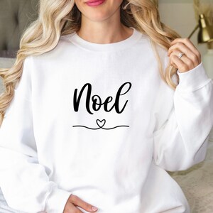 May include: White sweatshirt with the word "Noel" in black cursive lettering and a small heart above a line.