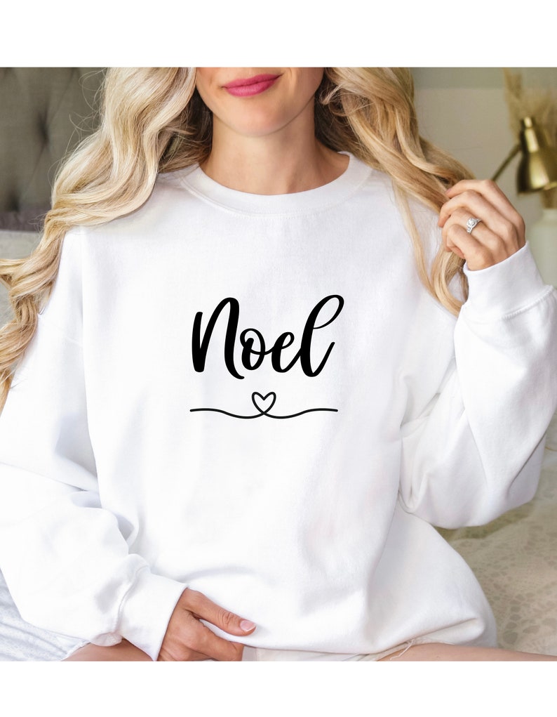 May include: White sweatshirt with the word "Noel" in black cursive lettering and a small heart above a line.