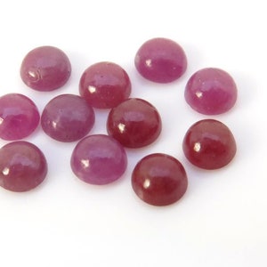 May include: A collection of ten round, cabochon-cut gemstones. The gemstones are a mix of pink and red hues.