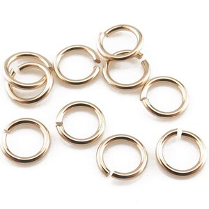 Puede incluir: Primer plano de diez anillos de salto dorados. Los anillos de salto son pequeños y redondos, y son perfectos para la elaboración de joyas.