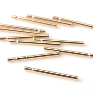 May include: A group of ten gold-colored metal rods, some of which are stacked on top of each other. The rods are about 1 inch long and have a smooth, shiny finish.