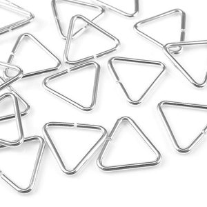 May include: A close-up of a group of silver triangle jump rings. The rings are scattered on a white surface.