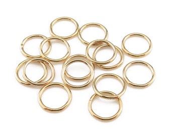 May include: A group of 12 gold jump rings, all the same size, arranged in a loose pile on a white background.