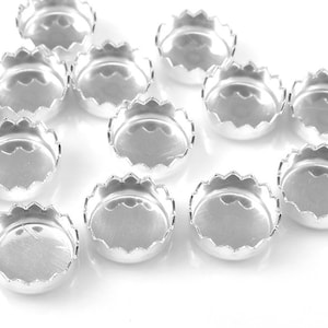 Puede incluir: Un grupo de 12 engastes redondos de metal plateado con forma de festón para la elaboración de joyas.