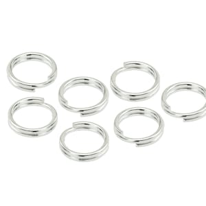 May include: Seven silver jump rings, each with a double loop, are arranged on a white background.