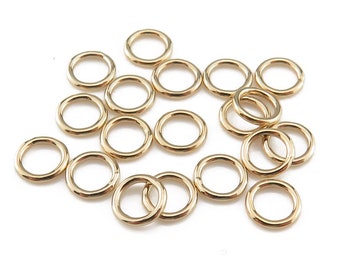 May include: A collection of gold jump rings, a type of jewelry finding, scattered on a white background.