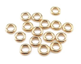 May include: A group of 15 gold jump rings, also known as split rings, are scattered on a white background. These rings are used for jewelry making and crafting.