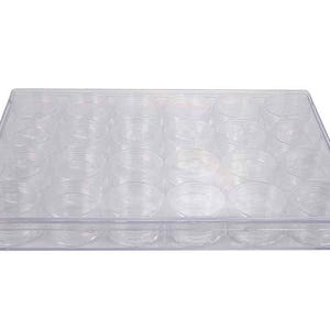 May include: A rectangular clear plastic storage case featuring twenty-four individual circular compartments arranged in a grid. The container has a transparent lid that covers all the small round jars, allowing for a clear view of the contents inside.