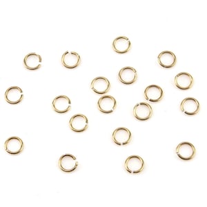 May include: A scattering of small, gold-coloured jump rings on a white background. The open rings are circular, with a small gap for attaching to other jewellery components. These are ideal for jewellery making and crafting.