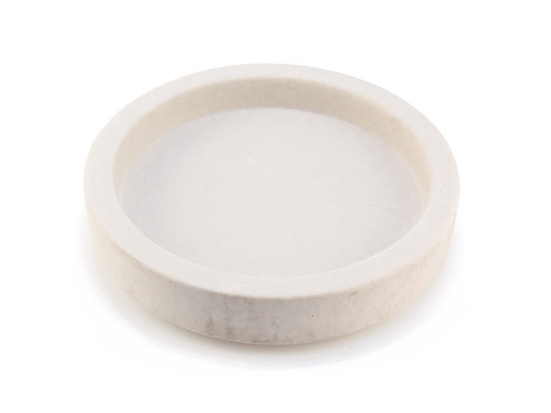 Op de afbeelding: Een ronde, witte keramische schaal met een licht verhoogde rand. De schaal is perfect voor het bewaren van kleine voorwerpen zoals sieraden of snuisterijen.