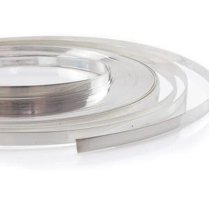 Può includere: Un rotolo di nastro metallico lucido color argento, avvolto strettamente. Il nastro è piatto e sembra essere fatto di un materiale riflettente, forse alluminio o un metallo simile. Sfondo bianco.