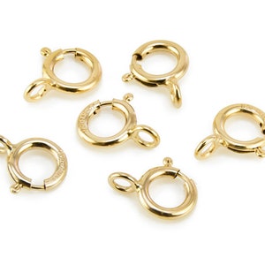 Puede incluir: Seis cierres de langosta de metal dorado, cada uno con un anillo circular y un pequeño gancho.