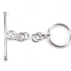 May include: A silver toggle clasp, comprising a straight bar with a rounded tip and a large ring. The clasp also has a series of linked rings. This jewellery finding is designed for the secure fastening of necklaces and bracelets.
