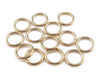 May include: A group of 12 gold jump rings, each with a smooth, rounded surface. The rings are arranged in a loose cluster, with some overlapping.