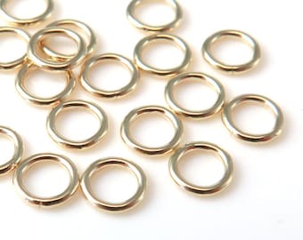 May include: A group of 15 gold jump rings, a type of jewelry finding, scattered on a white surface.