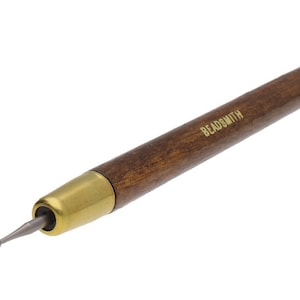 May include: A beading tool featuring a dark wooden handle and a brass-coloured metal ferrule. The tool's tip is a small, rounded metal point. The word "BEADSMITH" is printed on the handle. This tool is used for jewellery making and crafts.