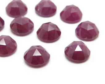 Pode incluir: Dez pedras preciosas de rubi facetadas, cada uma com uma cor vermelha profunda e um acabamento polido. As pedras preciosas estão dispostas em um padrão disperso sobre uma superfície branca.