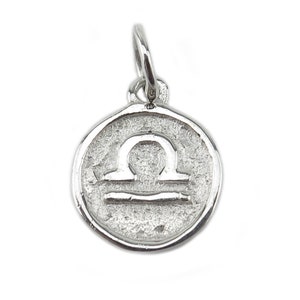 May include: Silver charm with a textured surface and the Libra zodiac symbol.