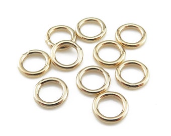 May include: A group of ten gold jump rings, all the same size, are scattered on a white background.