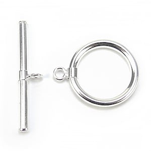 Könnte beinhalten: Ein silberfarbener Knebelverschluss, bestehend aus einem zylindrischen Stab und einem kreisförmigen Ring. Der Stab hat einen kleinen Haken, und der Ring hat eine Schlaufe zur Befestigung. Der Verschluss ist für die Schmuckherstellung konzipiert.