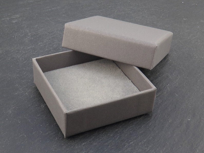 K&ouml;nnte beinhalten: Eine graue Pappbox mit grauer Filz-Auskleidung. Die Box ist ge&ouml;ffnet und der Deckel liegt auf der Seite.