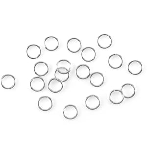 May include: A scattering of small, silver split rings on a white background. These circular metal rings are made of a shiny material. They are often used in jewellery making or for attaching items together. Each ring is approximately 1 cm in diameter.