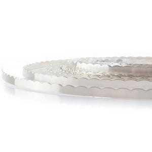 May include: Several silver-coloured metal bands with a scalloped edge. The bands are thin and appear to be made of a shiny metal. The edges have a repeating wave-like pattern. The bands are stacked on top of each other.