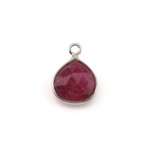 May include: A teardrop-shaped pendant featuring a faceted, deep red gemstone set in a smooth silver-toned metal bezel. The pendant includes a small circular jump ring at the top for attachment, showcasing a polished finish and a vibrant, dark crimson hue.