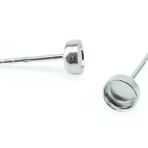 Könnte beinhalten: Zwei silberne Ohrring-Fassungen mit runden Zargen. Die Zargen sind leer und bereit, mit einem Cabochon gefüllt zu werden.