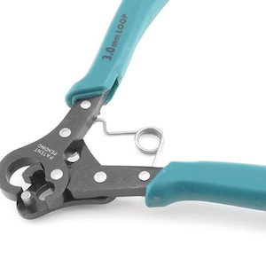 Può includere: Primo piano di uno strumento per la creazione di anelli in filo metallico con manici turchese. Lo strumento ha una molla e il testo "3.0mm LOOP" e "PATENT PENDING". Ideale per artigianato e gioielleria.