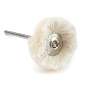 May include: A buffing wheel with a fluffy, off-white wool pad attached to a silver metal shaft. The pad is circular and has a metal center. The tool is designed for polishing and finishing surfaces.