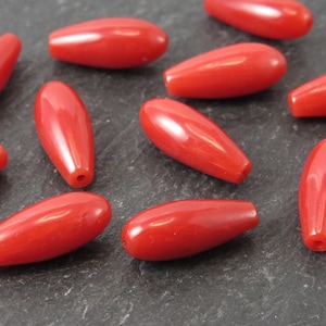 May include: A group of ten red, glossy, oval-shaped beads. The beads are smooth and have a slight shine.
