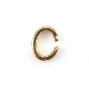 May include: A single, open gold-coloured jump ring, set against a white background. The ring is in the shape of a letter "C" with a small opening at the top. The metal has a slightly textured surface.