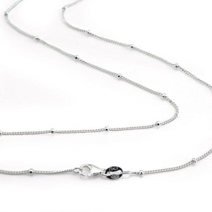 Può includere: Una delicata collana d'argento con piccole perline distanziate uniformemente. La catena è sottile e ha una chiusura a moschettone. La collana è esposta su uno sfondo bianco, evidenziando la sua semplice eleganza. La chiusura è contrassegnata "ITALY STERLING".