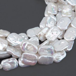 May include: Close-up of a collection of white, irregularly shaped freshwater pearls. The pearls have a lustrous, iridescent sheen, reflecting hints of pink, blue, and green. The background is a solid, dark grey, providing contrast to the bright pearls.