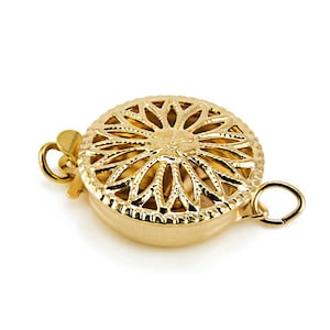 Puede incluir: Cierre de metal dorado con un diseño circular decorativo que presenta un patrón floral. El cierre tiene dos bucles para sujetarlo a un collar o pulsera.