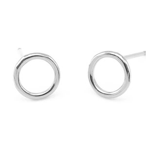 May include: A pair of silver circle stud earrings. The earrings are simple and minimalist, with a smooth, slightly textured finish.