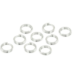 Puede incluir: Un conjunto de anillas partidas de color plateado, comúnmente utilizadas en la fabricación de joyas y artesanías. Las anillas están dispuestas sobre un fondo blanco, mostrando su forma circular y diseño dividido. Estos pequeños componentes metálicos son ideales para conectar varios elementos.