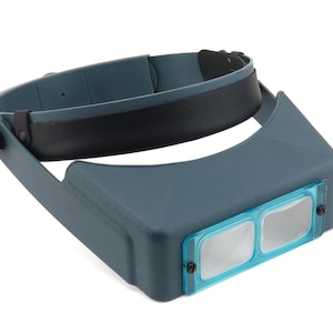 May include: A dark blue head-mounted magnifier featuring an adjustable headband with a black interior lining. The device includes a rectangular front frame with two clear lenses encased in a bright blue plastic border, secured by small black screws.