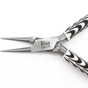 May include: A pair of silver-toned jewellery pliers with black and white swirl patterned handles. The pliers are labelled "the Bead Smith".