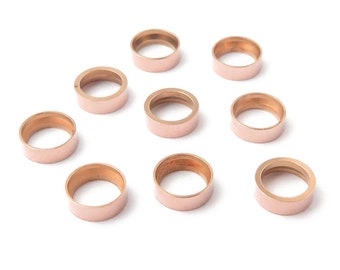 Può includere: Dieci anelli di salto in oro rosa, ognuno con una finitura liscia e lucida. Gli anelli sono disposti in un motivo sparso su uno sfondo bianco.