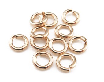May include: A group of ten gold jump rings, also known as split rings, are scattered on a white background. These rings are used for connecting jewelry components.