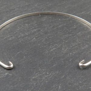 May include: A silver bangle bracelet with a simple, open design. The bracelet is made of a thin, round wire and has a smooth, polished finish.