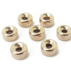 Puede incluir: Siete cuentas de metal de color dorado con un anillo central elevado. Las cuentas son redondas y tienen un acabado liso y pulido.