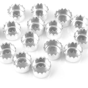 May include: A collection of silver-toned metal crown-shaped settings for jewelry making. The settings have a scalloped edge and a round center.